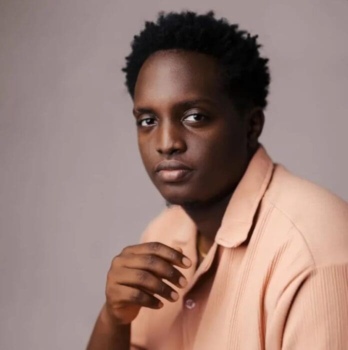 A person with short curly hair wearing a light peach shirt sits against a plain background, looking directly at the camera with a neutral expression, embodying 3Music’s spirit of bridging gaps in the creative community.