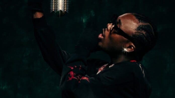 A person wearing black gloves and sunglasses stands in front of a microphone with a dark background, channeling the energy of Camidoh's "Ride Solo" featured on ghanamusic.com.
