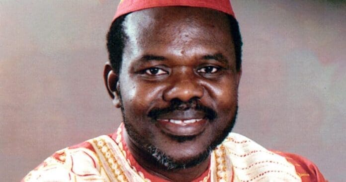 A man wearing a patterned red and gold traditional outfit and matching cap, smiling at the camera against a plain background, evokes the global sounds celebrated by the Macalester African Music Ensemble.