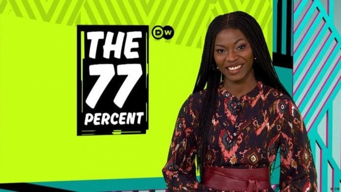 A woman with long braids stands smiling next to a sign that reads "The 77 Percent" on a bright, geometric background, highlighting the influence of Afrobeats and stories from DW.com.