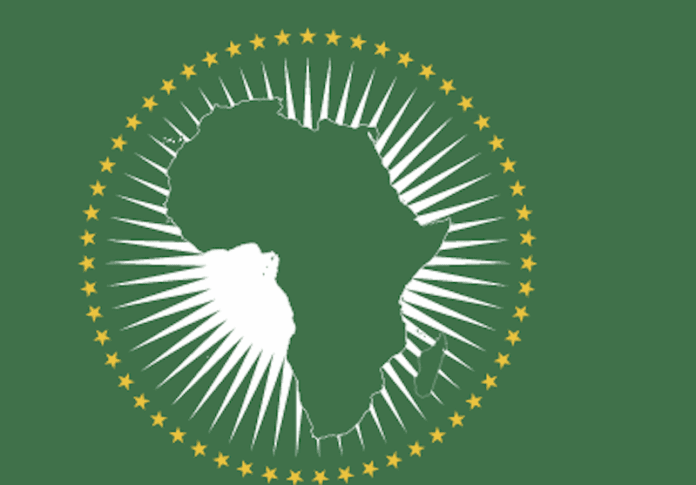 The image shows the emblem of the African Union (AU), featuring a green map of Africa surrounded by white rays and a circle of gold stars on a green background, symbolizing unity across events like AFRIMA and cities such as Lagos.