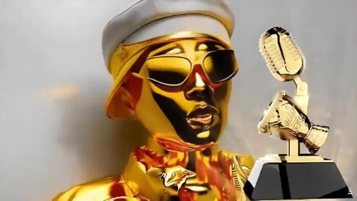 A person with gold skin, sunglasses, and a white hat poses beside a gold microphone-shaped trophy with a black base at the All Africa Music Awards in Lagos.