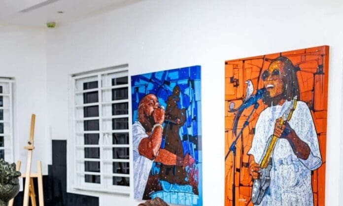 Two colorful paintings of musicians, inspired by Afrobeats, are displayed on a white wall near windows, with an easel and art materials visible in the background—creating a vibrant exhibition atmosphere.