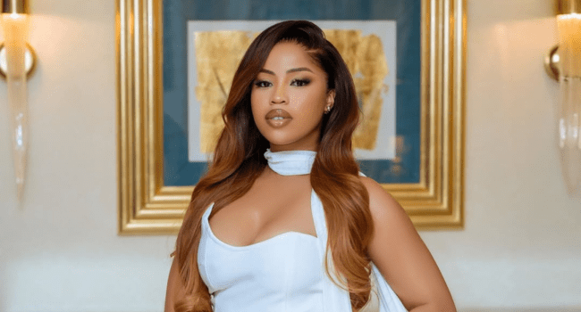 Anele Zondo, with her long, wavy brown hair and a white dress, stands indoors in front of framed artwork and wall sconces—captured just after a studio session for her new music release.