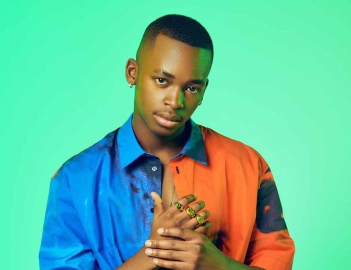 A young man with short hair, known as CIZA—the most streamed artist in South Africa—poses against a green background, wearing a colorful blue and orange shirt and several rings, with one hand resting on his chest.