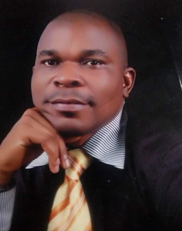 A man, reminiscent of Nigerian musician Fela Kuti, wears a striped-collar shirt and a yellow striped tie, posing with his hand on his chin against a plain dark background.