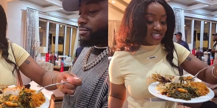 Two people indoors holding plates of food with rice, vegetables, and prawns, preparing to eat. Other people and kitchen items are visible in the background, creating a lively atmosphere reminiscent of Davido and Chioma’s marriage celebrations.