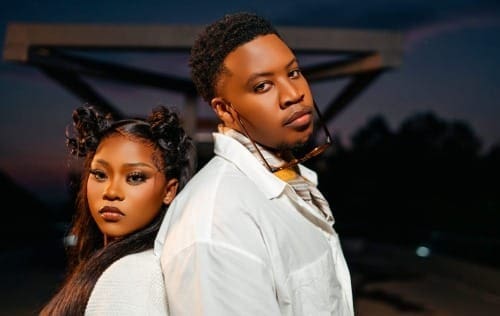 A woman and a man stand back-to-back outdoors at dusk, both wearing white outfits and looking toward the camera with serious expressions, capturing the mood of Mawelele by Naledi Aphiwe.