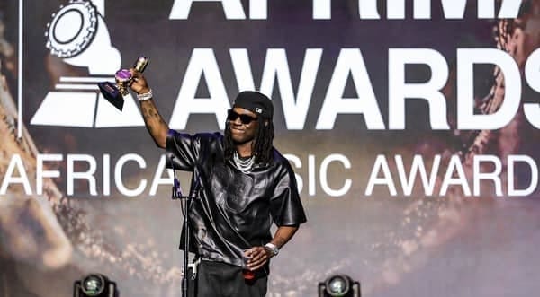 Rema, dressed in black leather, holds up a trophy on stage at the AFRIMA Africa Music Awards, celebrated by fans and covered by Peoples Gazette Nigeria.