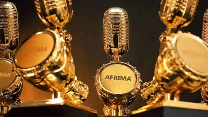 Several golden AFRIMA trophies shaped like microphones are displayed closely together, capturing the excitement of music fans at the AFRIMA Music Village.