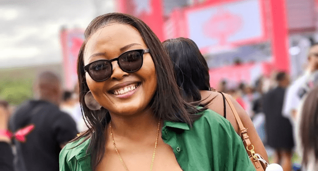 Woman wearing sunglasses and a green shirt smiles at an outdoor event, with blurred people and pink banners in the background at a 2016 SA Hip Hop gathering.