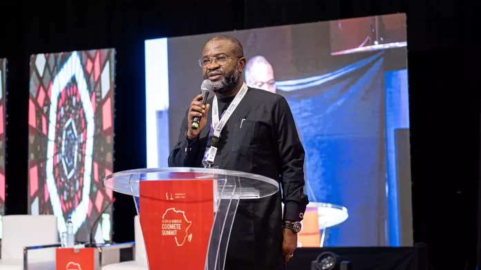 A man in a black outfit speaks into a microphone at a clear podium during the AFRIMA summit, discussing music growth and tech, with screens and event branding in the background.