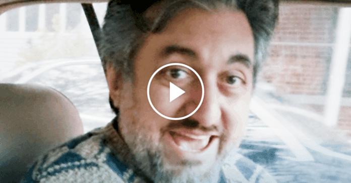 A middle-aged man with gray hair and a beard smiles while sitting in the driver’s seat of a car, reminiscent of a profile photo from the New York Times or an interview with a celebrated Nigerian musician.