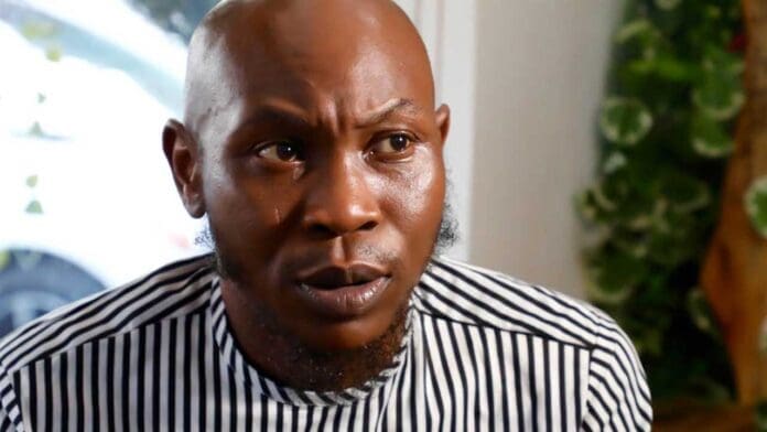 A man with a shaved head and a striped shirt looks to the side with a serious expression; greenery is visible in the background, reminiscent of Seun Kuti’s portraits featured in The Guardian Nigeria.