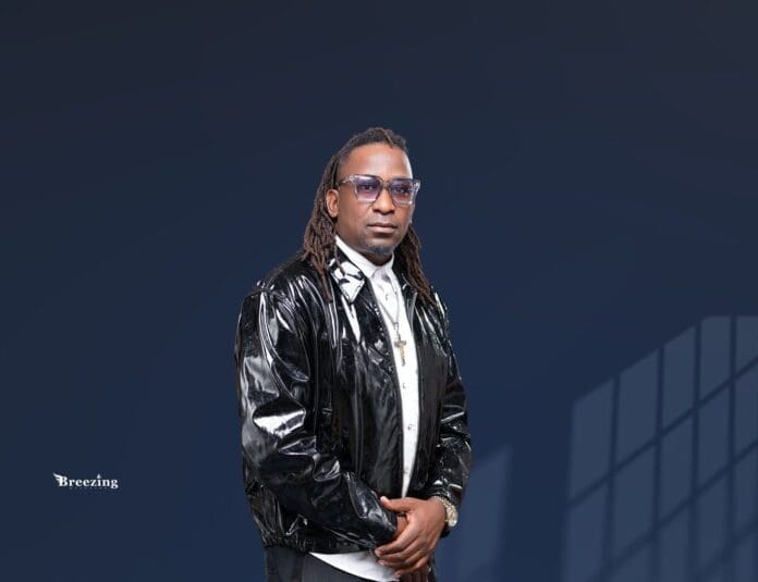 A man wearing glasses, a shiny black jacket, and a white shirt stands in front of a dark blue background with geometric window shadows, as if waiting for the music to start at an exclusive 24-hour buffet.