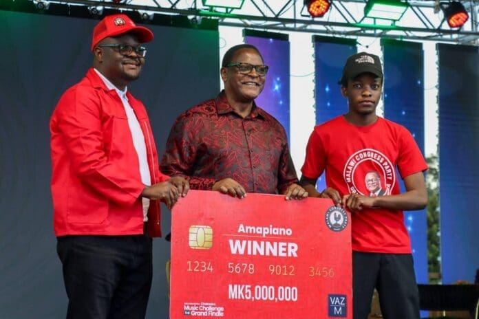 Three men stand on stage holding a large ceremonial cheque for MK5,000,000 labeled "Amapiano Winner," celebrating Emmanuel Harry's victory during a prize-giving event.