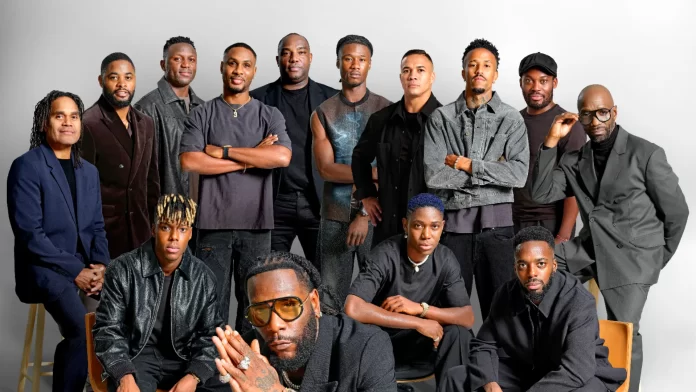 Fourteen men pose together against a plain background, most dressed in dark clothing, with some sitting and others standing in rows—an energetic, sporty group that could easily grace the cover of HYPE Magazine.