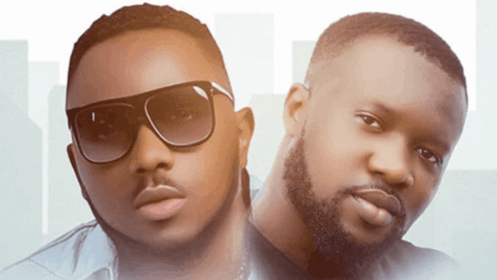 Two men pose side by side against a light background; one wears sunglasses and the other has a trimmed beard and mustache, capturing the vibrant spirit of GHF Media.