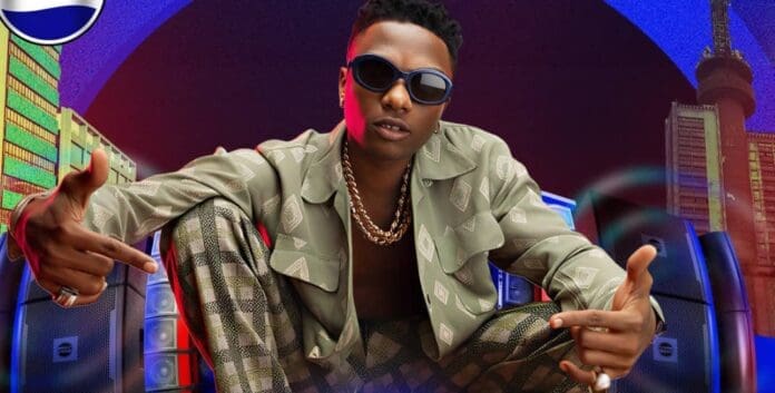 Person wearing sunglasses and patterned clothing sits in front of speakers, pointing fingers, with city buildings in the background and a Pepsi logo in the corner—channeling the vibe of top African artiste Wizkid known for racking up Spotify streams.