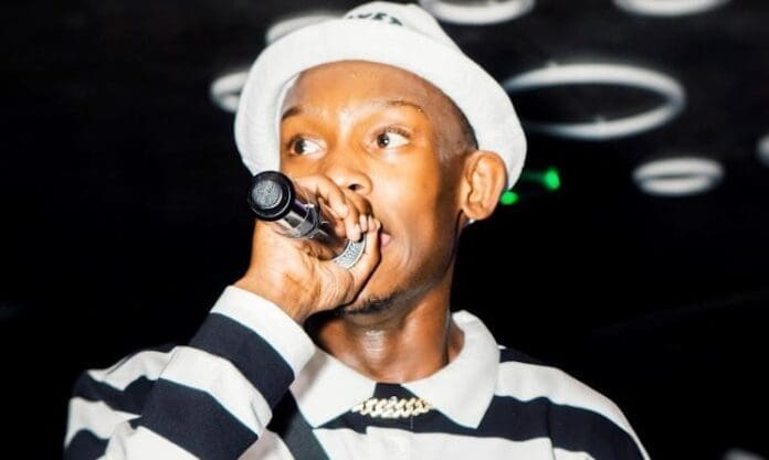 A person wearing a white hat and striped shirt holds a microphone and performs on stage under circular lights, capturing the vibrant energy of Music In Africa.