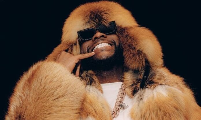 A person wearing a large fur coat and hood, sunglasses, and a thick chain necklace smiles and holds a hand to their face as if making a phone call gesture, channeling amapiano vibes like Davido.