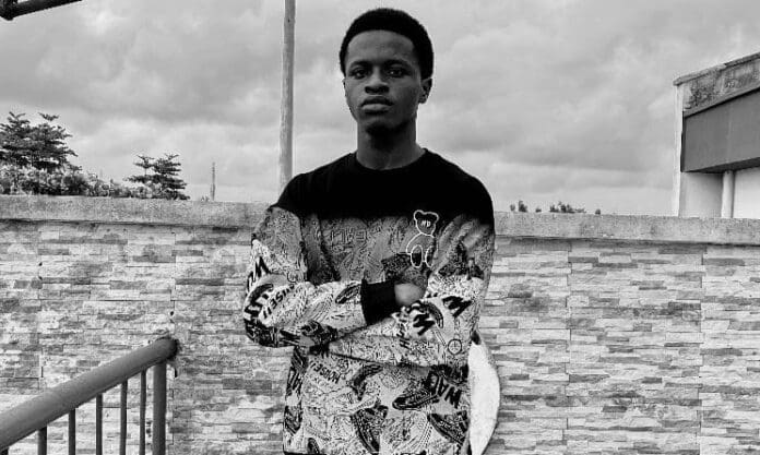 A young man stands with arms crossed in front of a stone wall outdoors, wearing a patterned sweatshirt; the black and white image captures the spirit of Africa’s next wave, echoing the energy of Music In Africa.