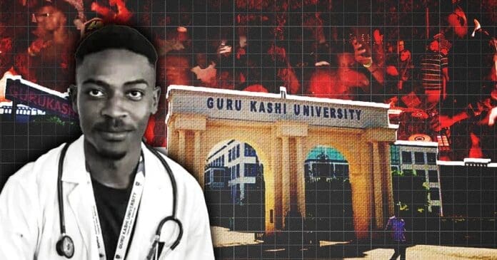 A man in a doctor's coat stands in front of an entrance labeled "Guru Kashi University" in India, with a crowd of people in the background.