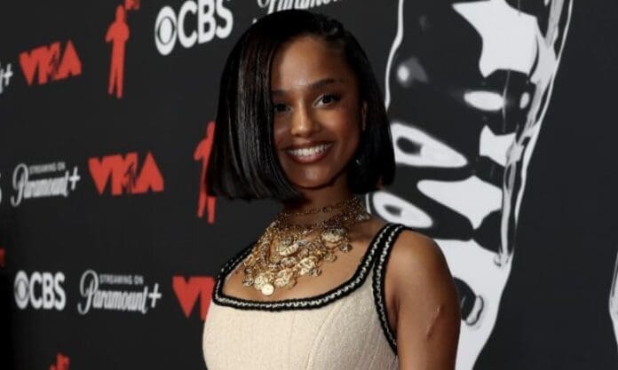 A woman with a sleek bob hairstyle and layered gold necklaces poses in front of a black and white backdrop featuring MTV Video Music Awards 2025 event logos.
