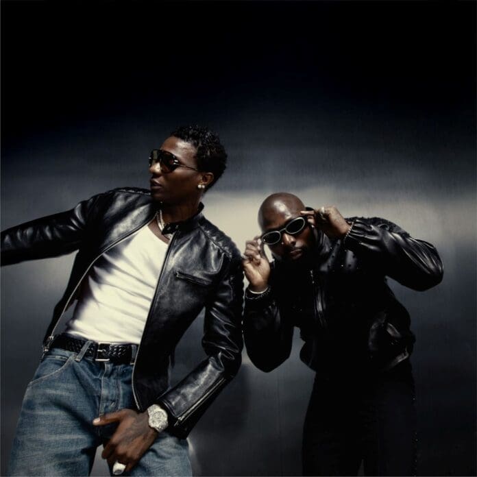 Two men in black leather jackets and sunglasses pose together against a dark background, channeling Asake and Wizkid vibes. One stands upright, while the other leans forward, adjusting his sunglasses.