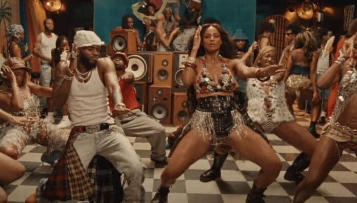 People dance energetically in a lively indoor setting, with speakers and onlookers in the background. The checkered floor reflects vibrant, fashionable outfits as OkayAfrica curates East African Songs for September 2025.