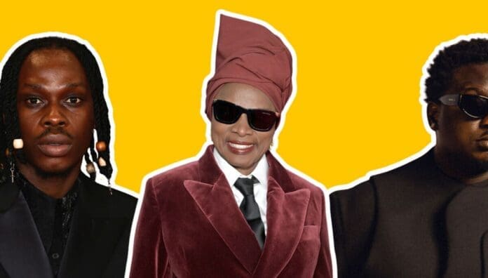 Three people in dark clothing and sunglasses pose against a bright yellow background; the central person wears a tall headwrap and maroon suit, channeling the bold style often celebrated by OkayAfrica and contemporary African artists.