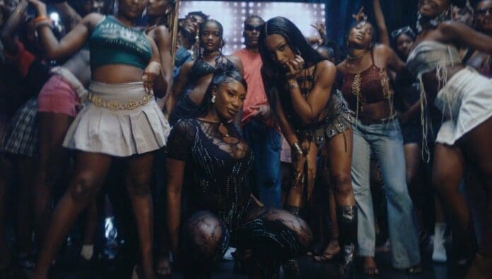 A group of people pose together at a party, with two women crouching in the front and others standing behind them; colorful outfits and a festive atmosphere inspired by Africa-Diaspora music collaborations.