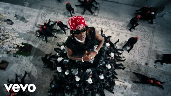 A man wearing a red bandana and a skirt of people channels the bold style often seen in Asake and Fireboy DML’s music videos.