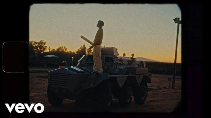 A person stands on top of a military armored vehicle at sunset in an outdoor setting, capturing a dramatic moment from the Seyi Vibez Official Video. The Vevo logo is visible in the bottom left corner.