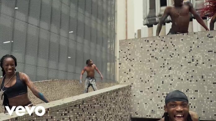 Four people, all shirtless or in swimwear, are smiling and climbing or running around tiled structures in an urban outdoor setting. The Vevo logo and “Chella Loyal Official Visualizer” appear in the bottom left corner.