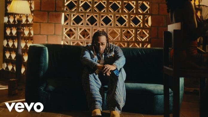 A man wearing sunglasses sits on a dark green sofa in a dimly lit room with patterned brick walls; the Vevo logo and "Very Soon" by BNXN appear in the corner.