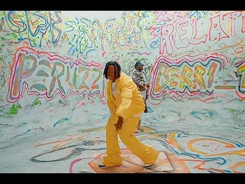 Two people in a brightly colored, graffiti-covered room; one, possibly inspired by Berri Tiga or Peruzzi, wears a yellow suit and dances in the foreground, hinting at a lively relationship between music and art.