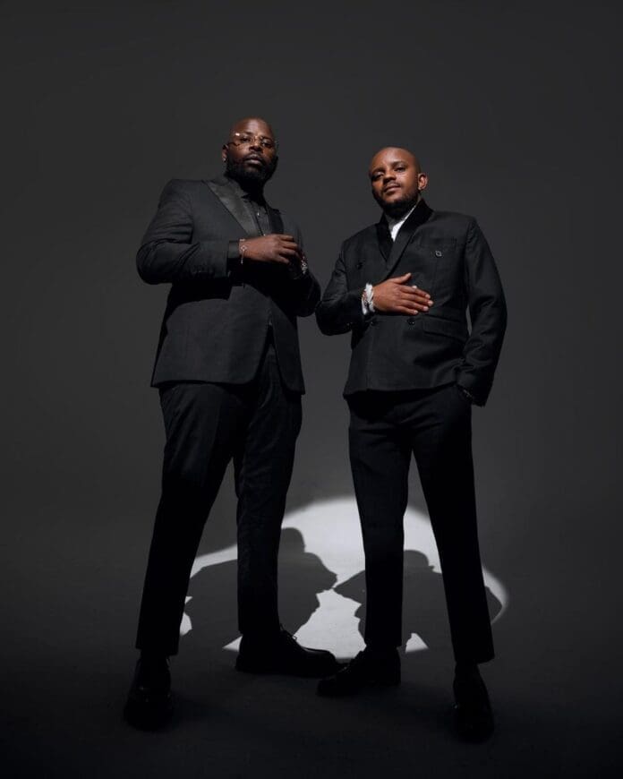 Two men in black suits stand confidently under a spotlight, facing the camera with serious expressions against a dark background—capturing the bold energy of amapiano duo Scorpion Kings at CTIJF.
