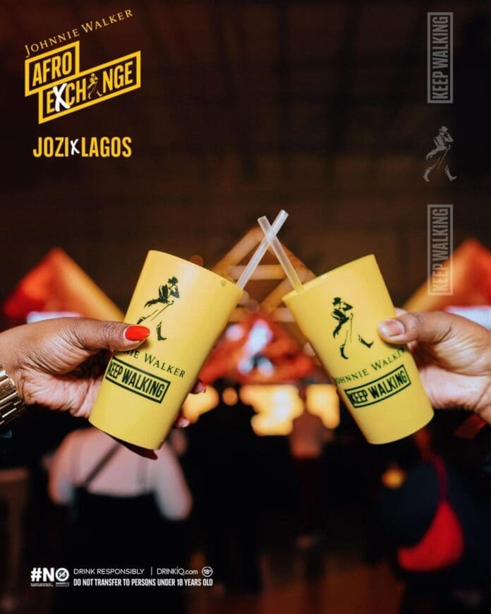 Two hands holding yellow Johnnie Walker cups clink together at the Johnnie Walker AfroExchange event. The background is blurred, with "JOZI x LAGOS" and "Keep Walking" branding–DJ Maphorisa sets the vibe.