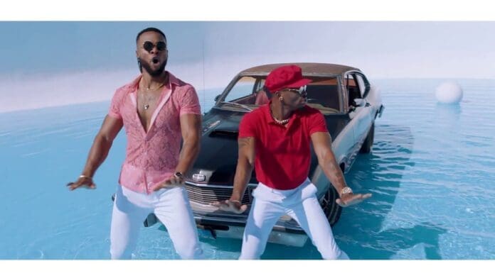Diamond Platnumz and Flavour, dressed in stylish outfits, dance in front of a classic car parked on a shallow, reflective blue surface with a white background in this vibrant Official Video.