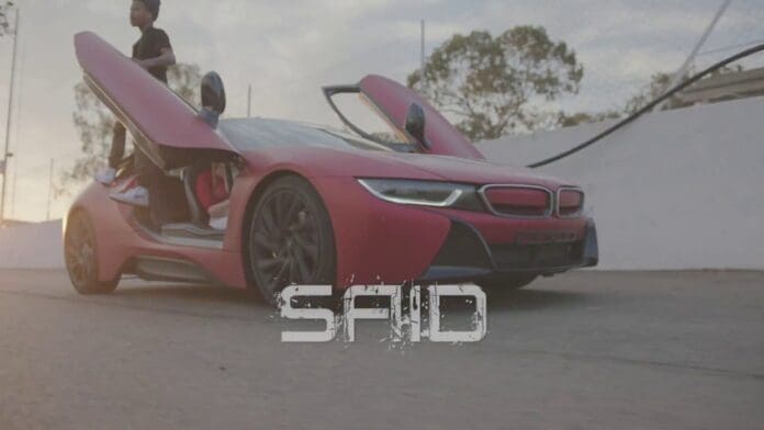 A red BMW i8 with gull-wing doors open is parked on a street, with a person standing next to it and the word "SAID"—inspired by Nasty C and Runtown's hit—overlaid on the image.