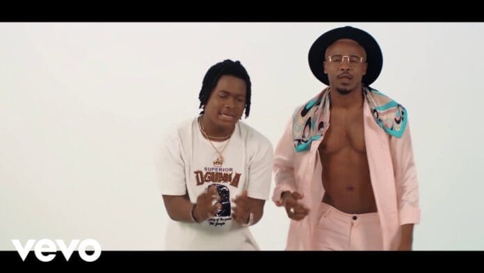 Alikiba and Singah stand side by side in a studio; one wears a white t-shirt, while the other sports a pink suit jacket, hat, and scarf with an open chest—ready for their "Somebody" collaboration.