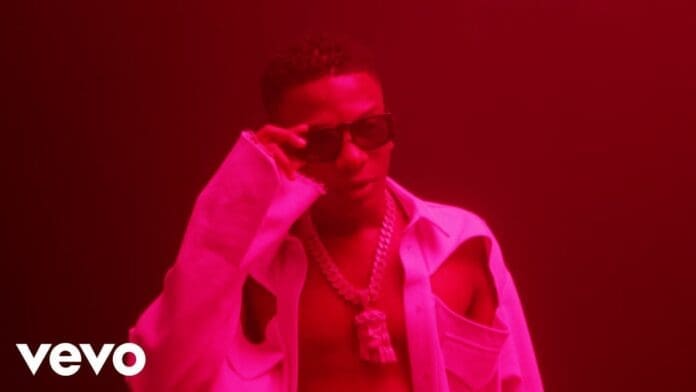 A person wearing sunglasses, a chunky chain necklace, and an open shirt poses under red lighting, channeling the cool Mood of a Wizkid or BNXN music video. The Vevo logo is visible in the bottom left corner.