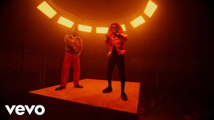 Two men, Wizkid and Burna Boy, stand on an elevated platform under orange lighting, with a circular light fixture above them in a dark room. The Vevo logo is in the bottom left corner.