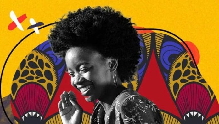 A woman with a natural afro hairstyle smiles, standing in front of a vibrant, colorful abstract background with bold patterns and yellow, red, black, and blue hues, radiating African pride.