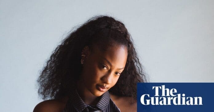 A woman with long, curly hair and a striped sleeveless top poses against a plain light background, representing the strength of women in music; The Guardian logo is in the lower right corner.