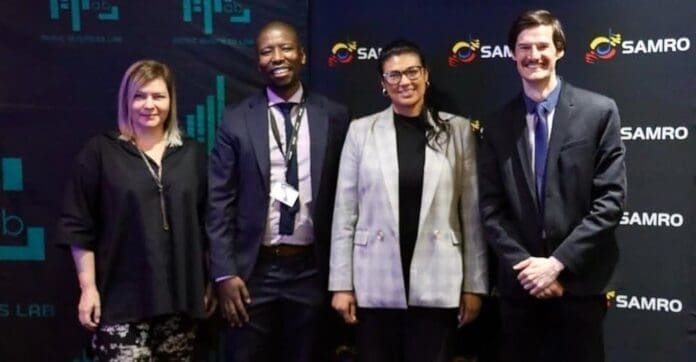 Four people stand side by side, posing for a photo in front of SAMRO and Bizcommunity logos. All are dressed in business attire, celebrating the Music Publisher Programme.