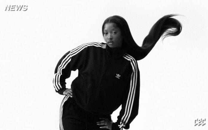A woman in a black Adidas tracksuit poses with one hand on her hip and her long hair swinging upward, channeling Uncle Waffles’ iconic Amapiano style against a white background.