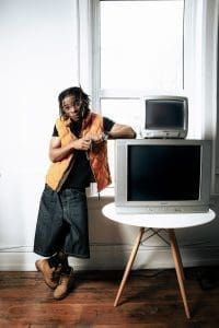 A man leaning on a table next to a television, listening to Afropop hits like "Go Through" by Yvng Chriis.