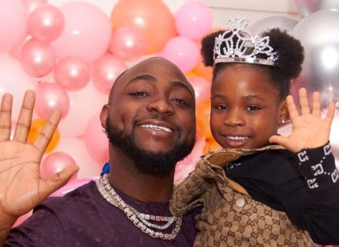 A man and a young girl, Imade, wearing a tiara smile and wave at the camera, with pink and white balloons in the background—capturing a joyful moment amid the ongoing custody case with Davido.